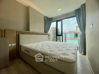 Modern bedroom with large window and city view, featuring a comfortable mattress and stylish decor.