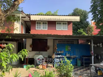 Charming two-story house with outdoor kitchen and lush greenery, perfect for family living.