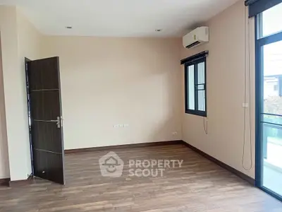 Spacious empty room with wooden flooring and large windows, perfect for customization.