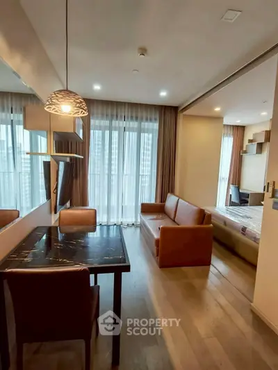 Modern living room with dining area and view into bedroom, featuring stylish furniture and large windows.