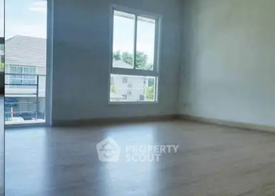 Spacious empty room with large window and wooden flooring, offering ample natural light and a serene view.