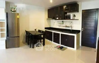 Modern kitchen with sleek cabinets, dining area, and stainless steel appliances in a cozy apartment.