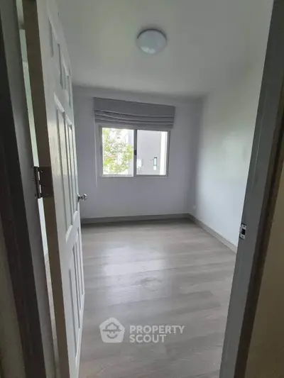 Bright empty bedroom with large window and wooden flooring, perfect for customization.