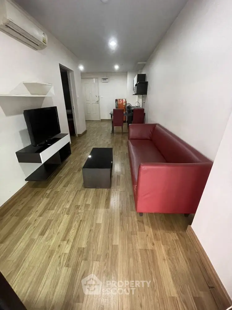 Modern living room with red sofa, TV, and wooden flooring in a cozy apartment setting.