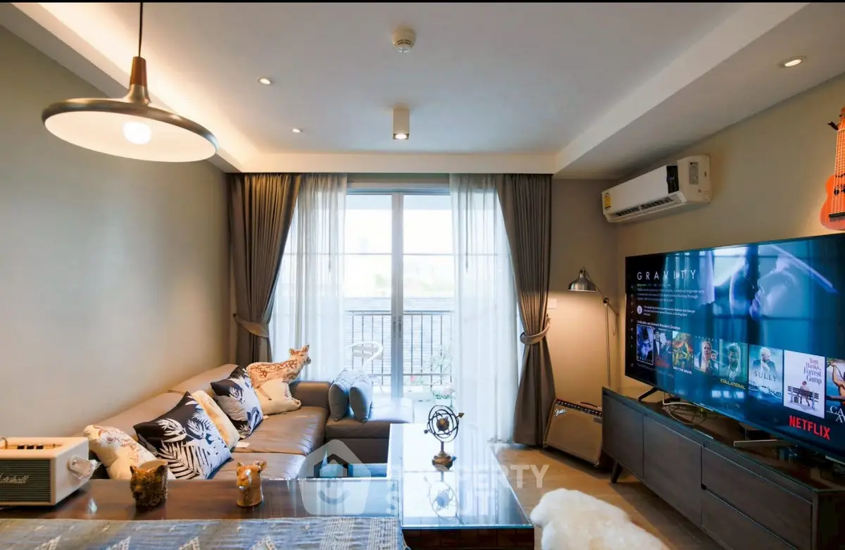 Modern living room with large TV, cozy sofa, and balcony view