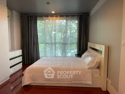 Spacious bedroom with large window and modern decor, offering a serene view of lush greenery.