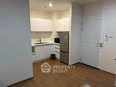 Modern compact kitchen with white cabinets and stainless steel fridge in cozy apartment