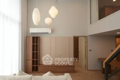 Modern living room with high ceiling, stylish pendant lights, and elegant wooden furniture.