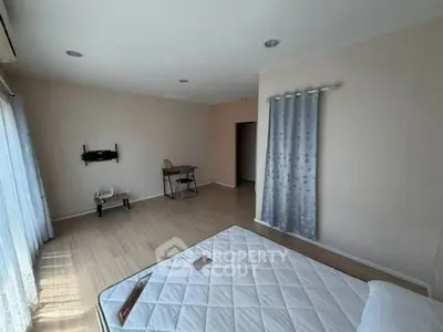 Spacious bedroom with natural light and minimalist decor, featuring a mounted TV stand and wooden flooring.