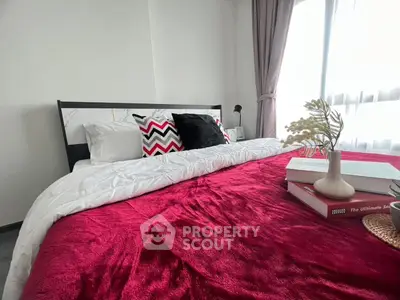 Cozy bedroom with stylish decor and natural light, featuring a plush red blanket and elegant pillows.