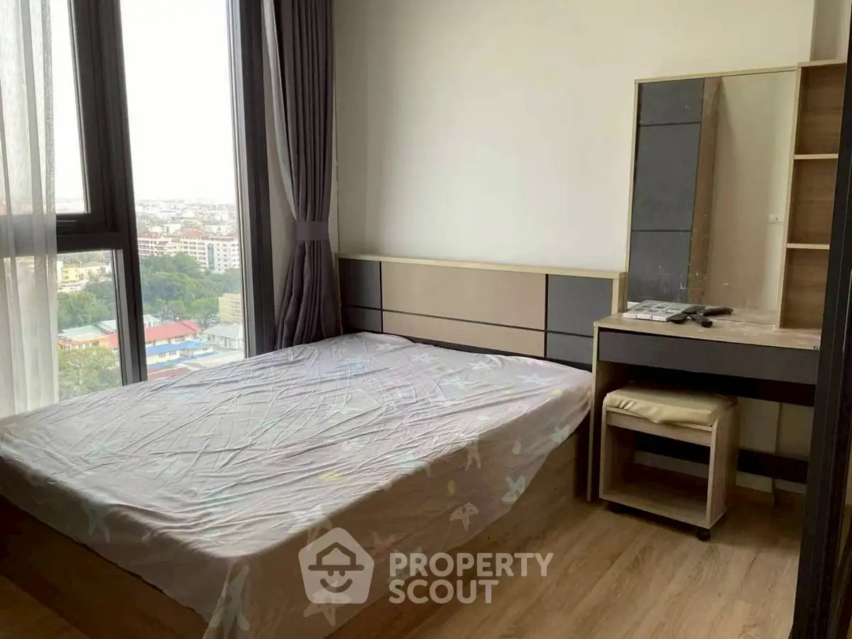 Cozy bedroom with large windows and city view, featuring modern furniture and natural light.