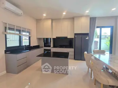 Modern kitchen with sleek cabinetry, black countertops, and dining area in a bright open layout.
