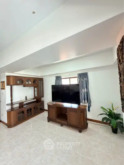 Spacious living room with elegant wooden furniture and large TV, perfect for relaxation and entertainment.