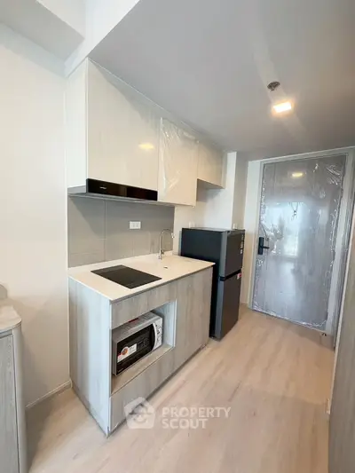 Modern kitchen with sleek cabinetry, compact fridge, and built-in microwave in a stylish apartment.