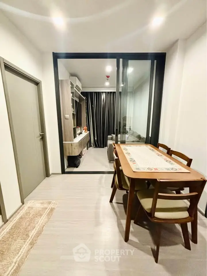 Modern dining area with wooden table and chairs, adjacent to a cozy living room with glass partition.