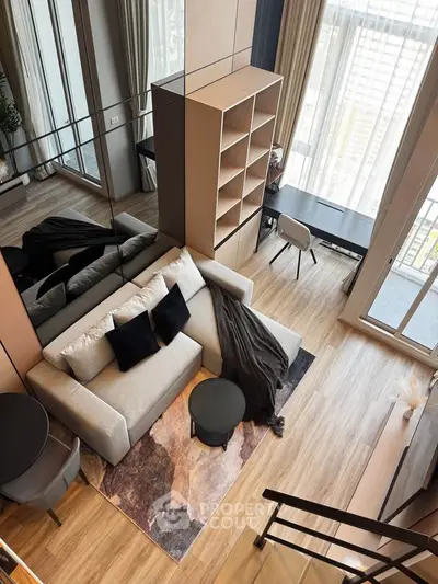 Modern living room with high ceilings and large windows, featuring stylish furniture and a cozy atmosphere.