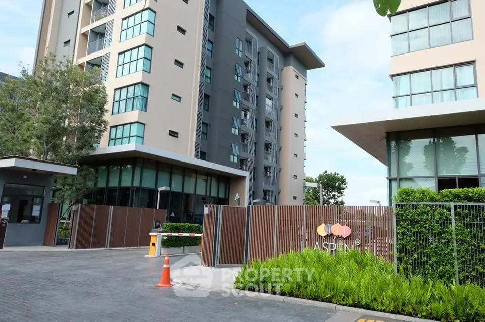 Modern apartment building entrance with lush greenery and secure gate access.