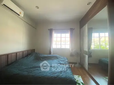 Cozy bedroom with large window and mirrored wardrobe, featuring air conditioning and wooden flooring.