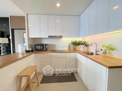 Modern kitchen with sleek white cabinets and wooden countertops, featuring a compact oven and stylish decor.