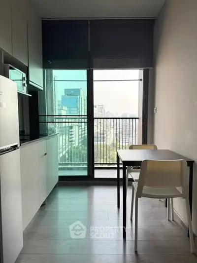 Modern kitchen with sleek design and city view from large window, featuring compact dining area.