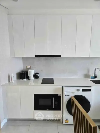 Modern kitchen with sleek white cabinets, built-in microwave, and washing machine.