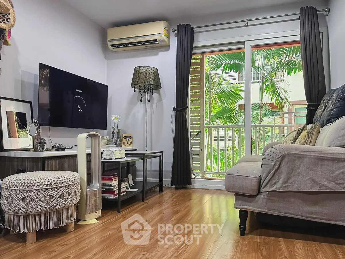 Cozy living room with modern decor, air conditioning, and a view of lush greenery through large windows.