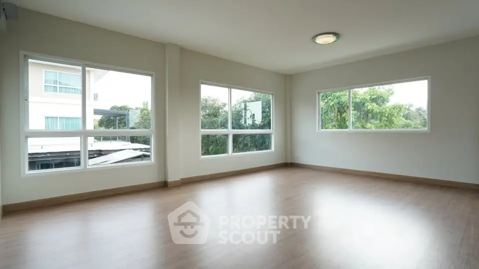 Spacious empty room with large windows and wooden flooring, offering abundant natural light and serene views.