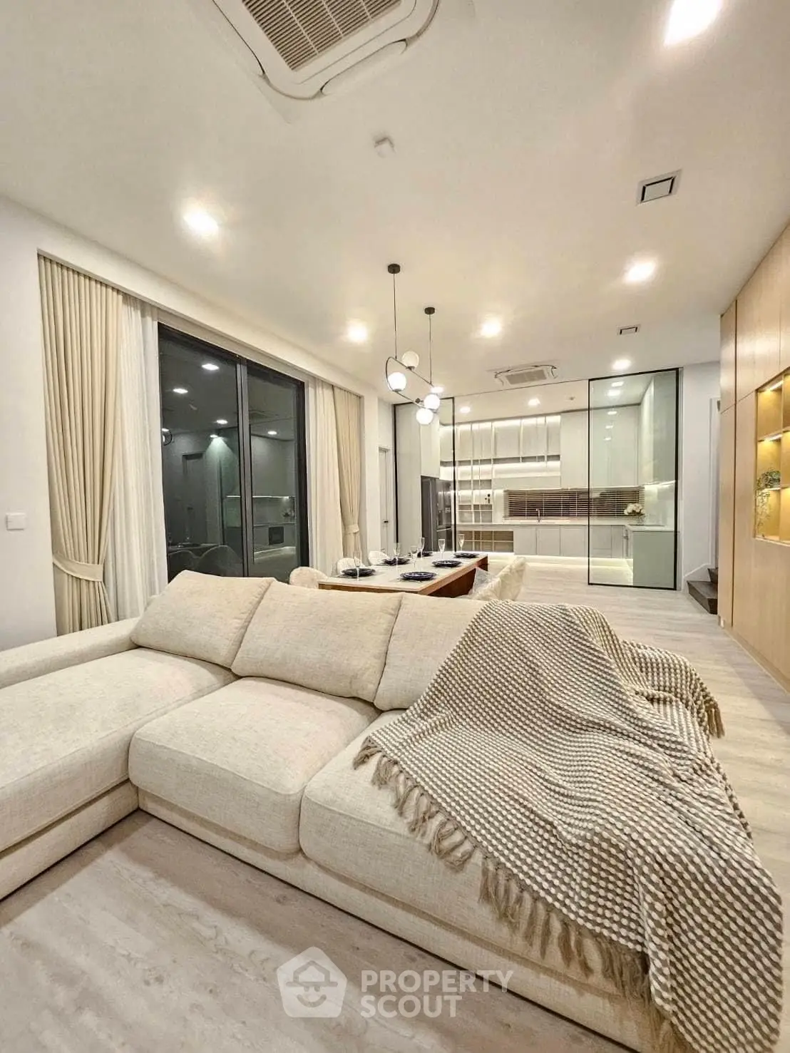 Luxurious modern living room with open kitchen, elegant lighting, and cozy beige sofa.