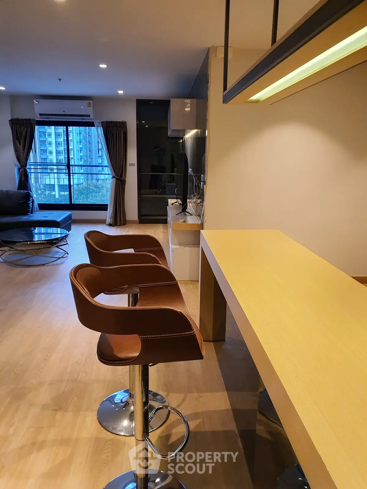 Modern open-plan living room with stylish bar stools and large windows offering city views.