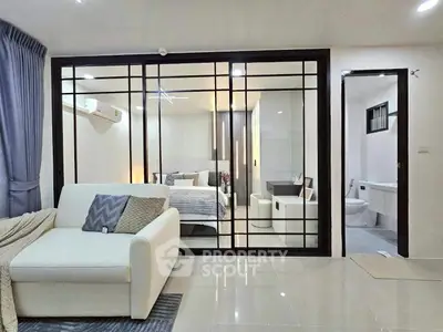 Modern living room with glass partition leading to a stylish bedroom, featuring sleek furniture and elegant decor.