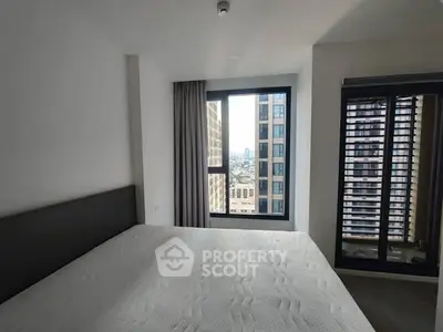 Modern bedroom with city view and large windows in high-rise apartment.