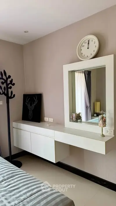 Modern bedroom with stylish decor and wall-mounted clock, featuring a sleek vanity and elegant lighting.