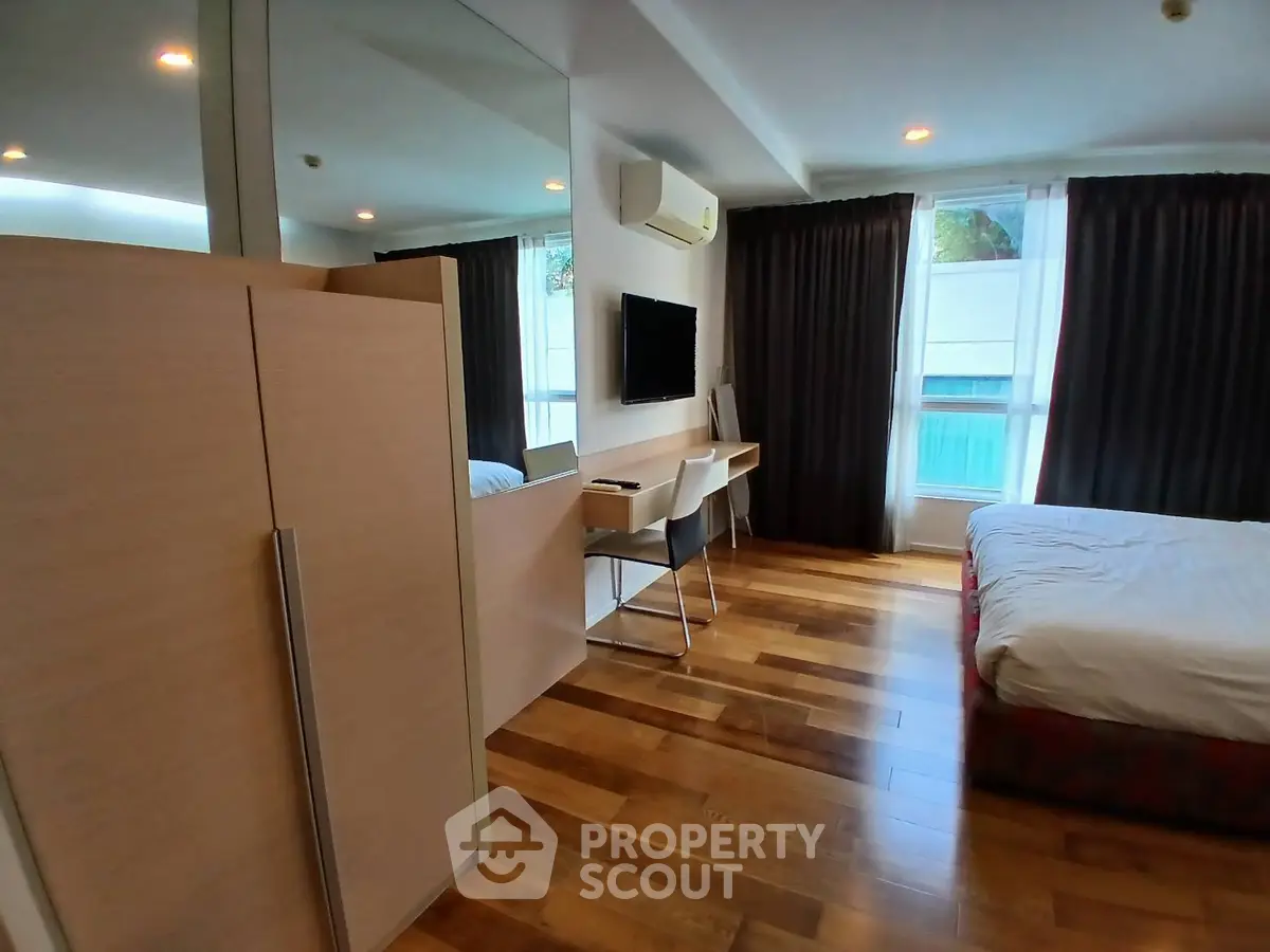 Modern bedroom with wooden flooring, large window, and sleek furniture