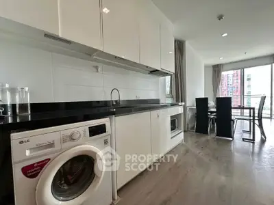 Modern kitchen with sleek cabinetry and in-unit washing machine, open layout to dining area with city view.