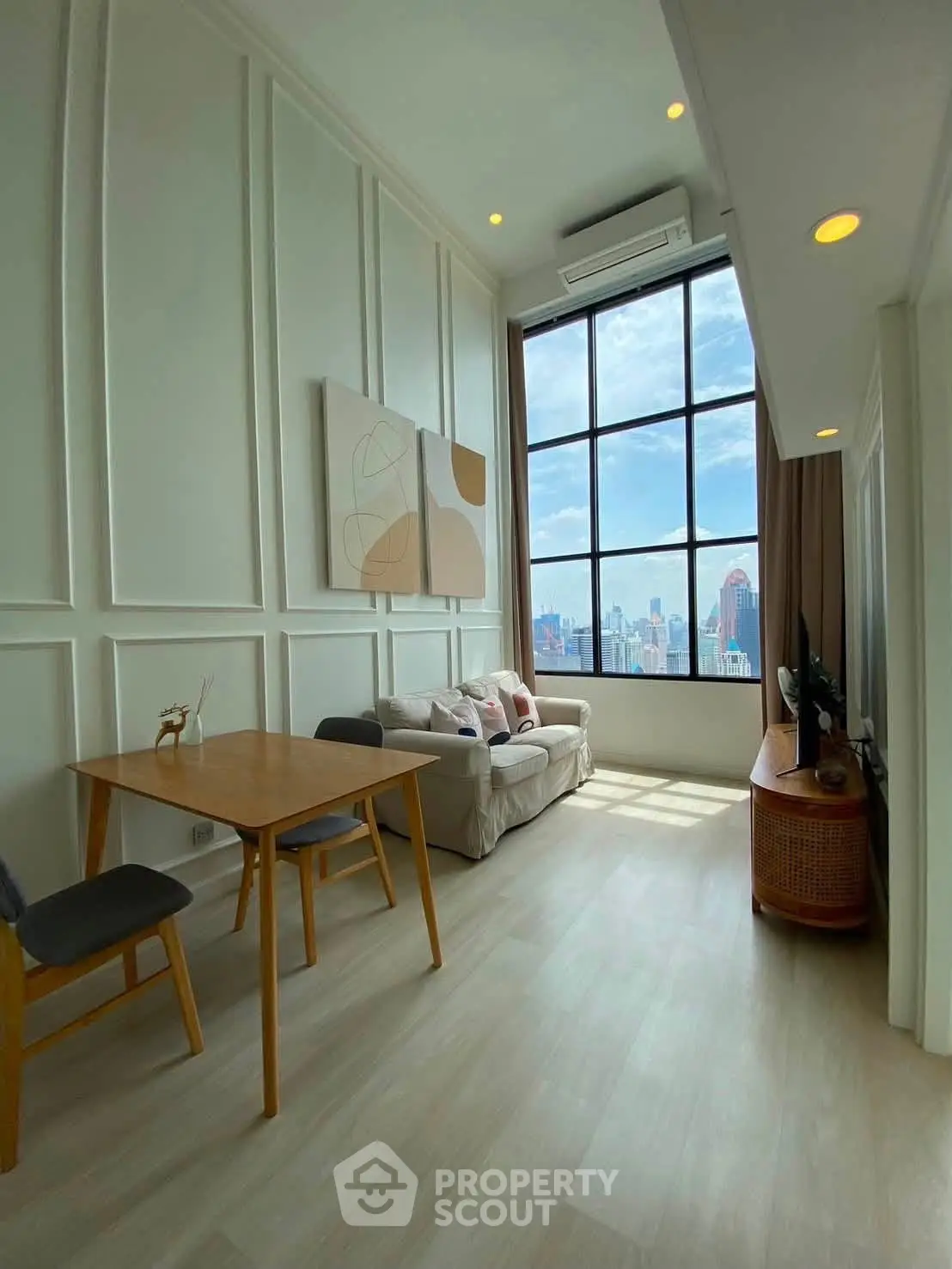 Spacious living room with high ceilings and city view, featuring modern decor and large windows.