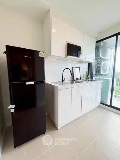 Modern kitchen with sleek black fridge and white cabinetry, featuring a scenic balcony view.