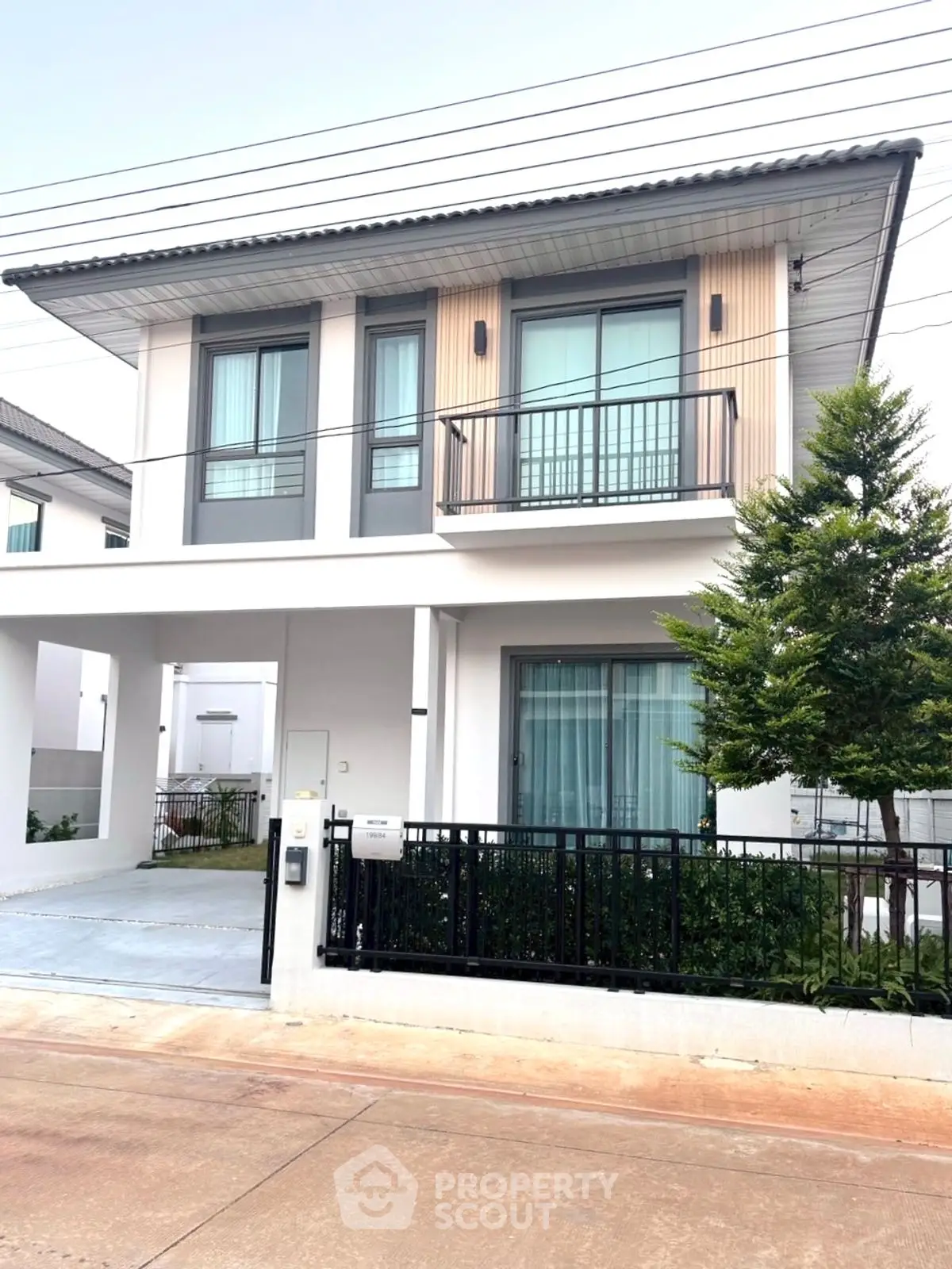 Modern two-story house with balcony and driveway in a suburban neighborhood.
