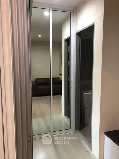 Modern apartment hallway with mirrored closet doors and view into living room.