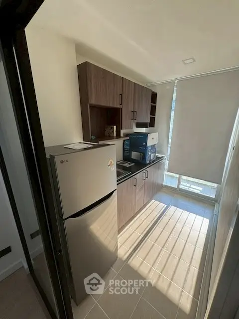 Modern kitchen with sleek cabinetry and natural light, featuring a compact fridge and appliances.
