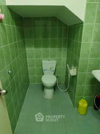 Compact green-tiled bathroom with toilet and sink, ideal for efficient space use.