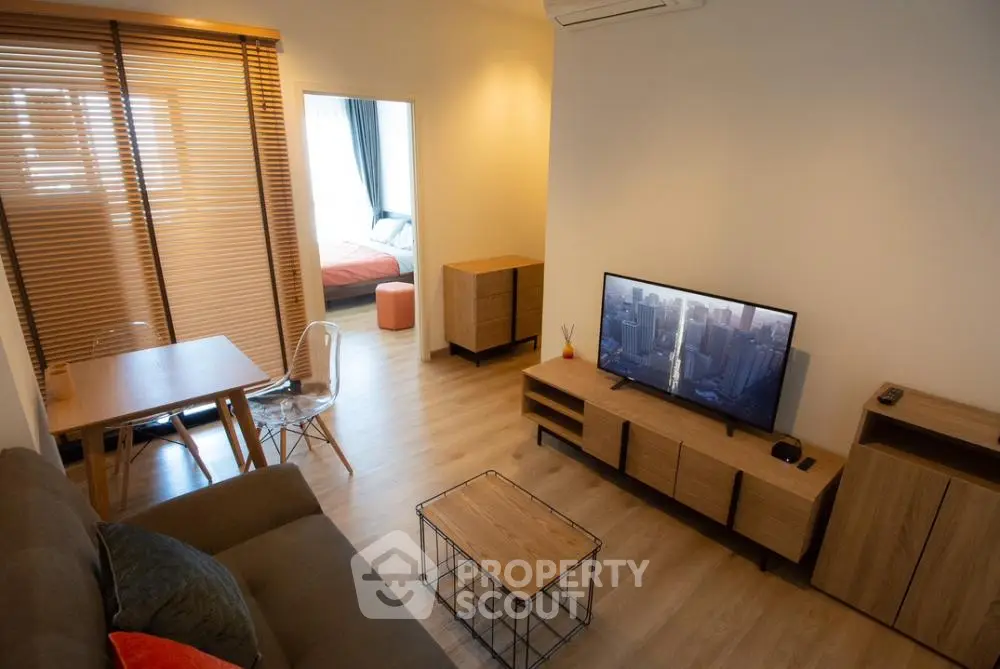 Spacious modern living room with ample natural light, featuring a cozy sofa set, flat-screen TV, and a dining area that seamlessly connects to a comfortable bedroom space.