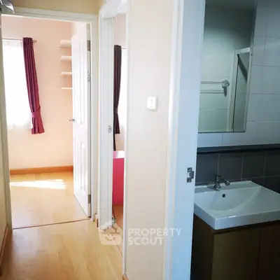 Bright hallway leading to a cozy bedroom and modern bathroom with sink.
