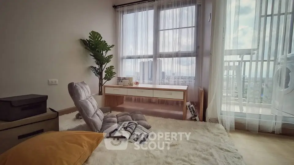 Cozy living room with plush carpet, floor seating, and large windows offering a stunning city view.