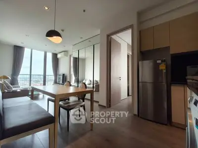 Modern open-plan living room with dining area and kitchen, featuring floor-to-ceiling windows and stylish decor.