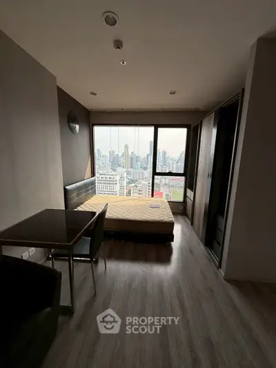 Modern studio apartment with city view, featuring a cozy bed and dining area.
