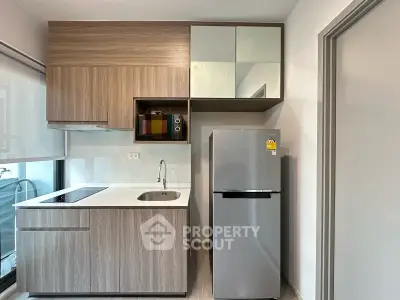Modern compact kitchen with sleek cabinetry and stainless steel fridge in a stylish apartment.