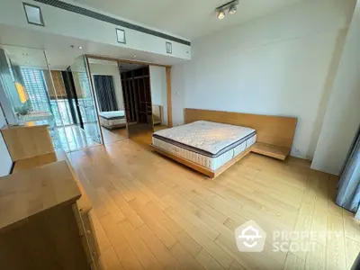 Spacious modern bedroom with wooden flooring and large mirrored closet in luxury apartment.