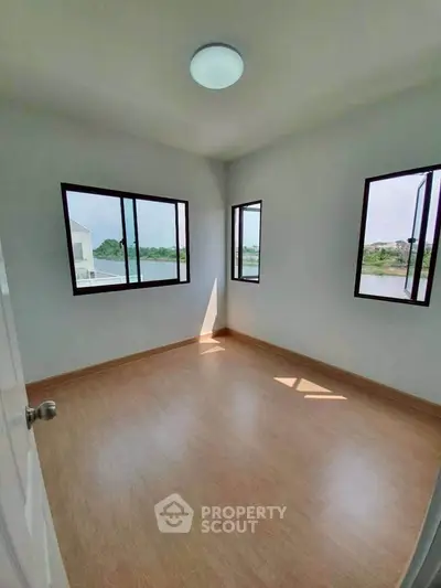 Bright empty room with large windows and wooden flooring, offering a serene view, perfect for customization.