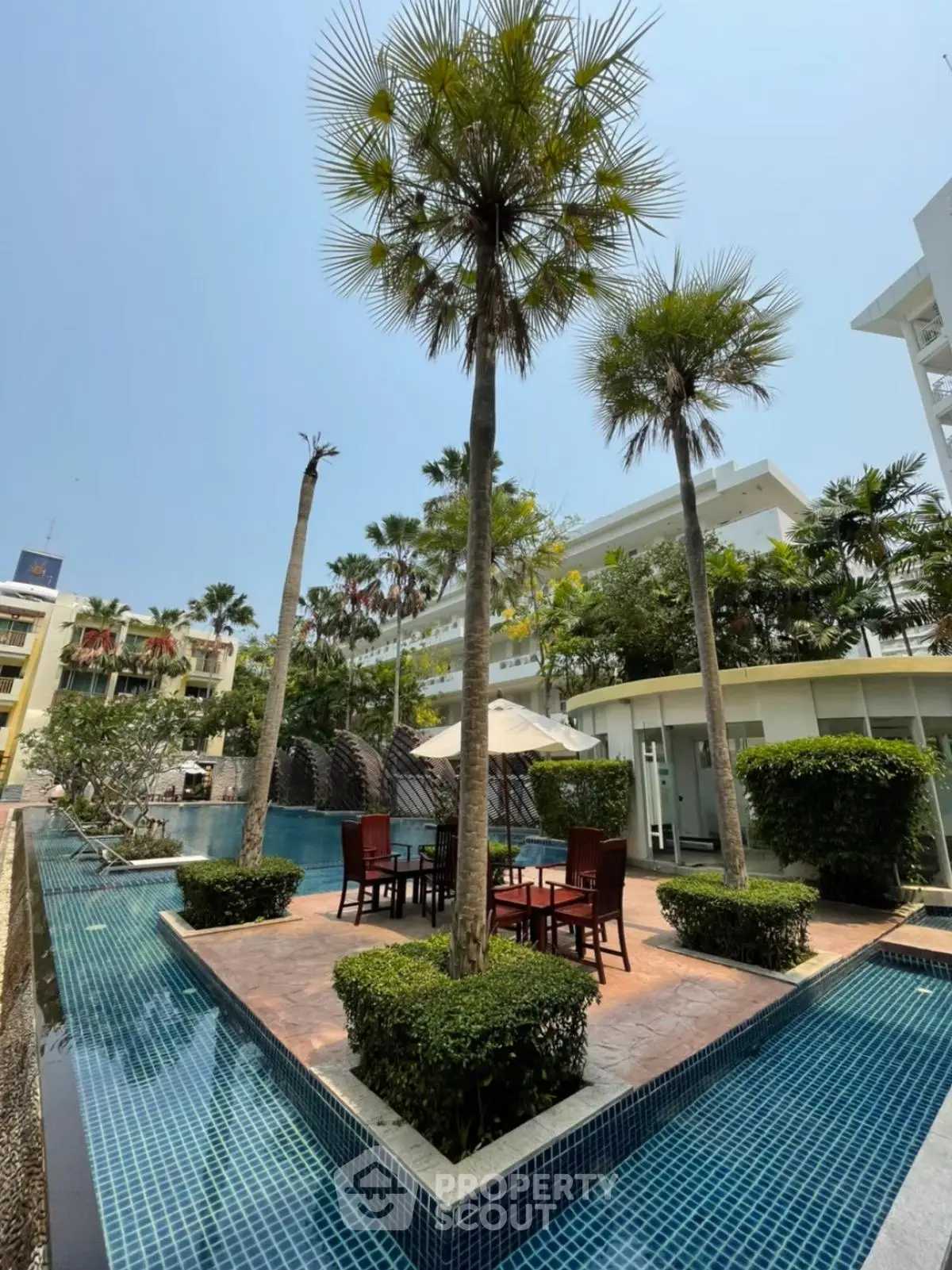 Luxurious outdoor pool area with palm trees and seating in a modern residential complex.