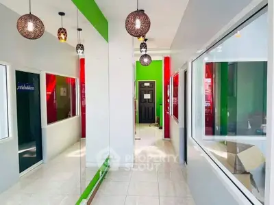 Modern corridor with vibrant green and red accents, stylish pendant lights, and large windows.